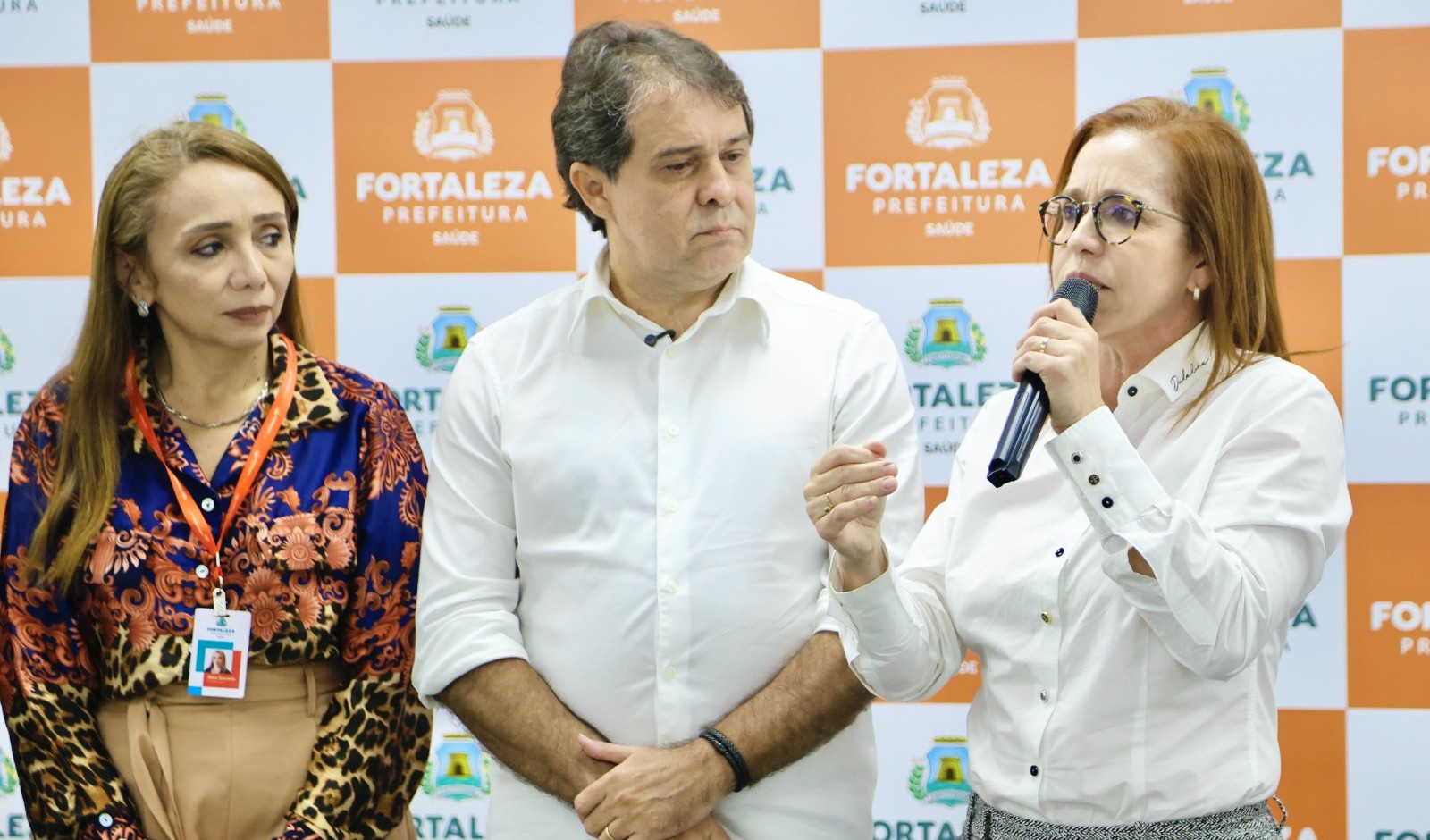 dra. riane azevedo fala ao microfone enquanto o prefeito evandro observa